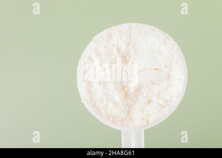 Whey protein powder in measuring spoon close up on green background, top view Stock Photo