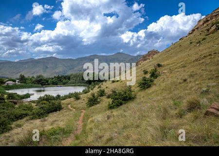 Footpath leading down a mountain side towards a small lake. In the background are mountains Stock Photo