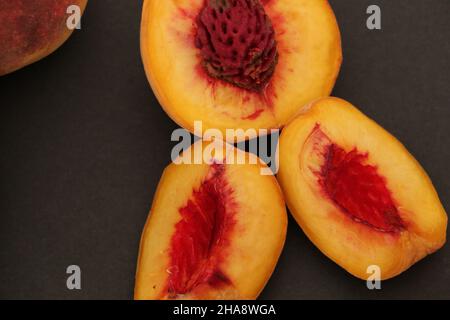 Fresh peaches stand on a black background.  Sliced ​​peaches are seen next to all the peaches. Stock Photo