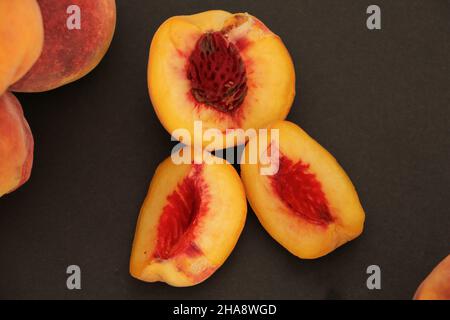 Fresh peaches stand on a black background.  Sliced ​​peaches are seen next to all the peaches. Stock Photo