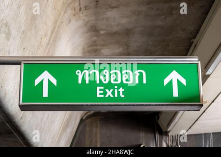 Emergency exit symbol glowing green in the blacked out background in English and Thai language Stock Photo