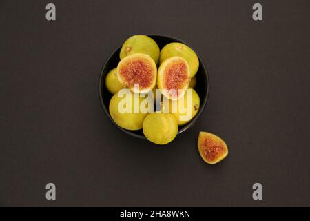 Green figs, figs in a black bowl.  Black background .  Some of them are sliced ​​and the seeds stand out. Stock Photo