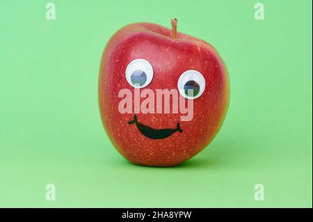 red apple with wiggle eyes on green background Stock Photo
