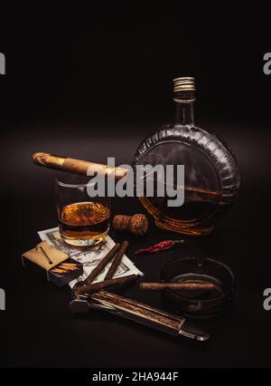 Quality cigars with cognac, cutter, 100 dollar paper, ashtray and red hot pepper on black background Stock Photo