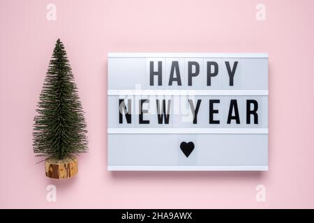 Green cristmas tree with lightbox with text HAPPY NEW YEAR on pink background. Minimal Christmas or New Year concept. Stock Photo