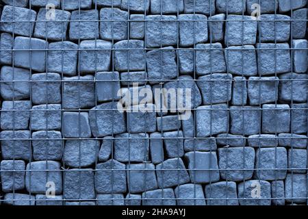 Gray-blue stone gabion of rectangular stone. Metal mesh with large cells. Abstract texture. Stock Photo