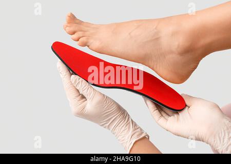 Orthopedist with red insole and female foot on light background, closeup Stock Photo