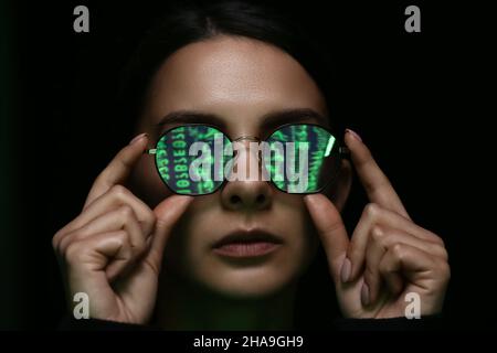 Woman with reflection of matrix code in her tinted glasses on dark background Stock Photo