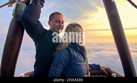 Adventure love couple on hot air balloon watermelon. Man and woman kiss hug love each other. Burner directing flame into envelope. Fly in morning blue Stock Photo