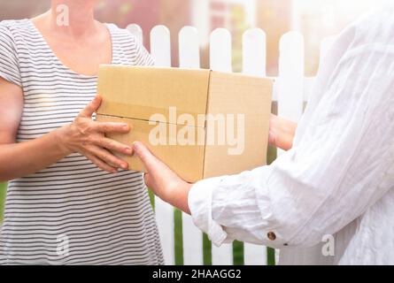 Woman courier handing the parcel to senior woman in front of the house Stock Photo