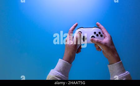 Male hands hold a gamepad on a blue background, copy space. Stock Photo