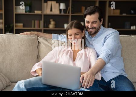 Joyful happy married couple relaxing at laptop on couch Stock Photo