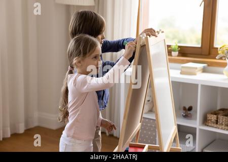 Two cute sibling kids drawing on toy small childish whiteboard Stock Photo