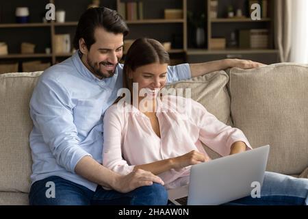 Happy cheerful millennial couple watching video, movie on laptop computer Stock Photo