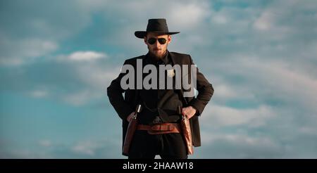 Sheriff in black suit and cowboy hat, banner. Wild west, western, man with vintage pistol revolver and marshal ammunition. Stock Photo