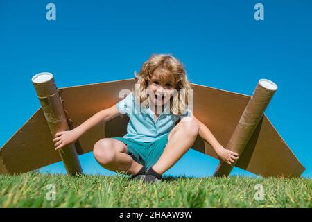 Happy child playing in park. Kid having fun with toy paper wings. Stock Photo