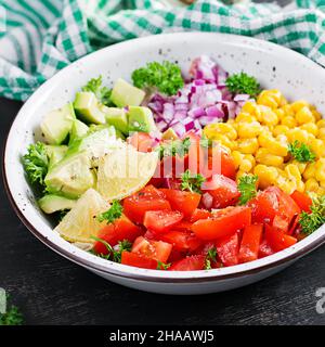 Salad with avocado, tomatoes, red onions and sweet corn in bowl. Vegetarian buddha bowl. Vegan food. Stock Photo
