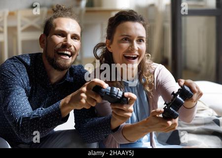 Happy joyful millennial couple enjoying virtual battle Stock Photo