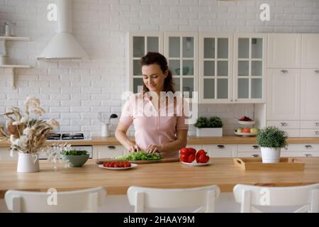 Happy homeowner woman cutting vegetables for salad in home kitchen Stock Photo