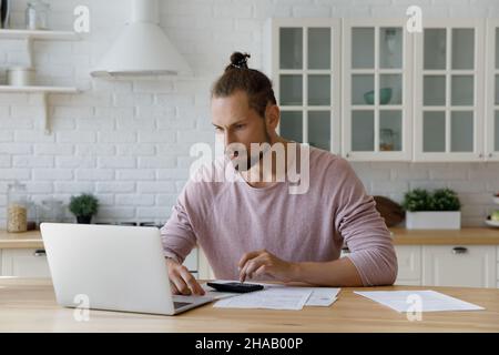 Focused bearded young hipster tenant man calculating mortgage fees Stock Photo