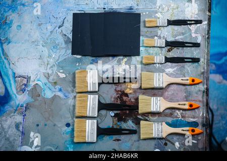Flat lay top view of brushes for painting on a messy stained table. Three sets of similar size. Stock Photo