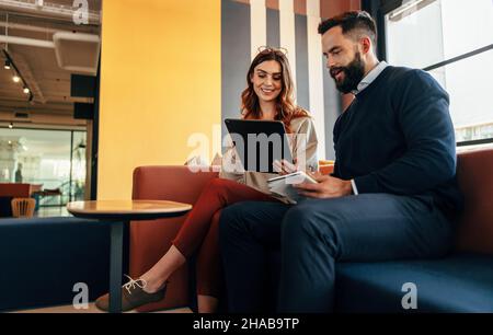 Happy businesspeople working together in an office lobby. Two modern businesspeople using a digital tablet in a co-working space. Two young entreprene Stock Photo