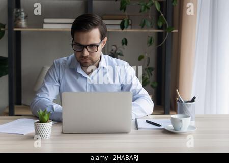 Young serious businessman sit at desk working on laptop Stock Photo