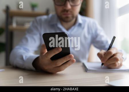 Man sit at desk holds pen, smartphone writing in notepad Stock Photo