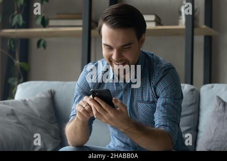 Smiling young man sit on couch with smartphone Stock Photo