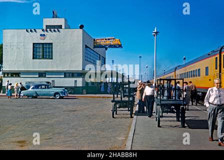 A busy scene at the railroad station at Las Vegas, Nevada USA in 1956 – a Union Pacific train has arrived at the platform. The ‘Streamline Moderne’-style train station was constructed in 1940, and upgraded with neon lights in 1946 (note the distinctive neon sign in the shape of a yellow railway engine on the building). The station served several Union Pacific trains a day, connecting to Los Angeles in the west and Salt Lake City, then Chicago and St. Louis in the east. This station was demolished in 1971 – a vintage 1950s photograph.