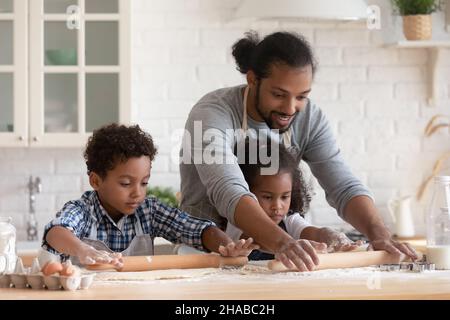 Loving African father teach children flattening dough for pastries Stock Photo