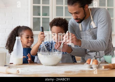 Loving African dad teach kids cooking in kitchen Stock Photo