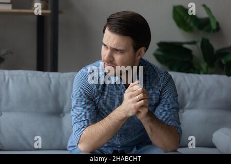 Man having mental pain, sit on sofa looks into distance Stock Photo