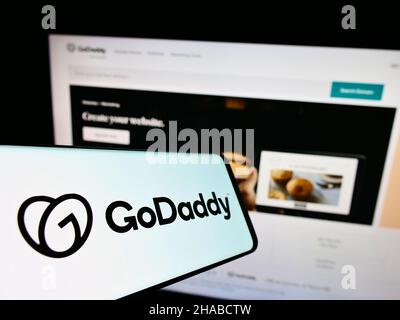 Cellphone with logo of American web hosting company GoDaddy Inc. on screen in front of business website. Focus on center-left of phone display. Stock Photo