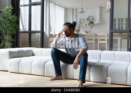 African guy sit on sofa touch head looks desperate Stock Photo