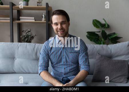 Smiling young man sit on sofa looking at camera Stock Photo