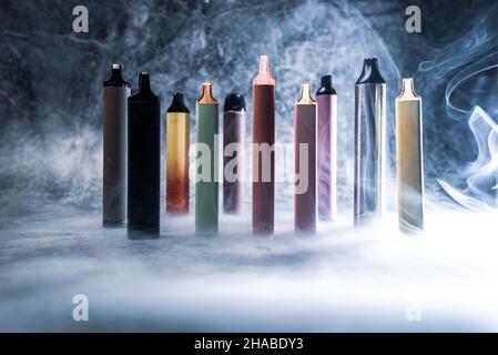 multicolored electronic cigarettes vape on dark background with smoke Stock Photo