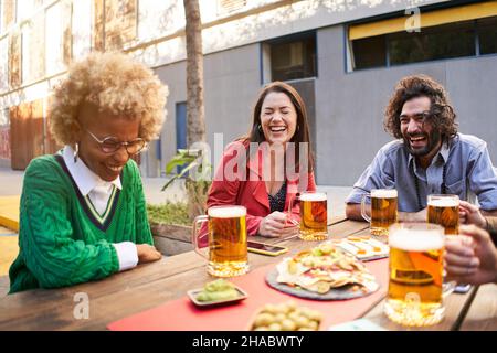 Group of friends drink beer and laughing on the terrace outdoors. Stock Photo