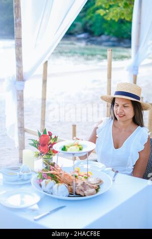 Romantic dinner on the beach in Phuket Thailand, woman mid age Asian woman having dinner on the beach in Thailand during sunset.  Stock Photo