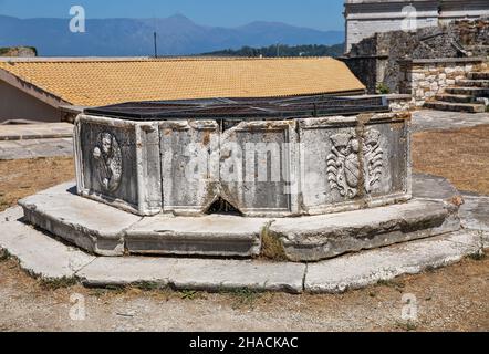 Ancient water well with Coat of arms in famous touristic landmark Old Venetian Fortress inner yard. Kerkyra city, Corfu, Greece Stock Photo