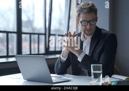 Brooding concentrated German businessman in formal suit and glasses sitting in office Stock Photo