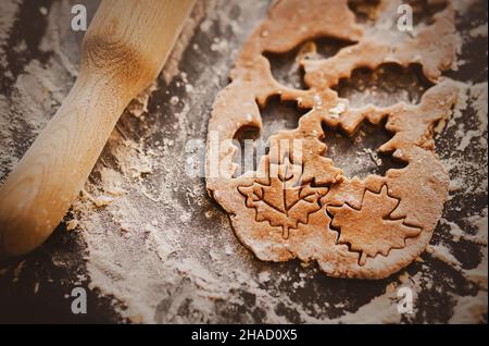 On a baking sheet sprinkled with flour, there is a dough from which gingerbread figures in the form of leaves are cut out. Sweet pastries in the autum Stock Photo