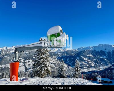 Artificial snow making machine in the Alps. The green artificial snow gun  is against a deep blue sky Stock Photo