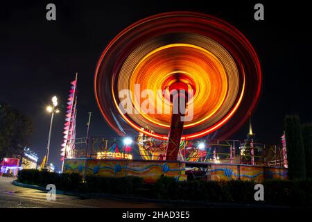 Photo of a carousel at night in a long exposure in an amusement park. The yellow and redder tones of the carousel bulbs merge in motion and give the i Stock Photo