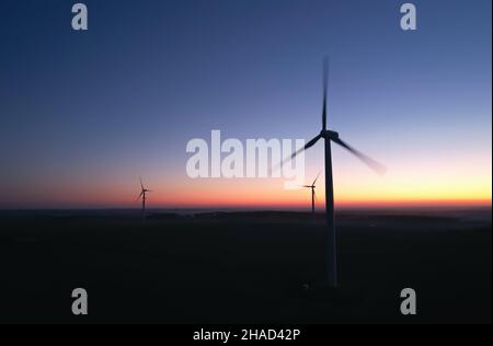 Three silhouettes of rotating propellers of wind turbines against the background of the night sky. Stock Photo