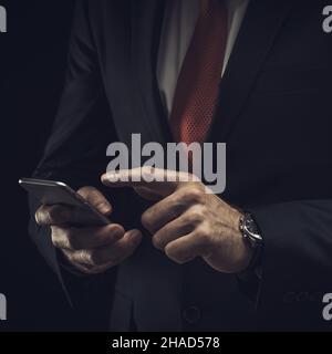 A businessman in a dark suit and a white shirt, on a black background, with a smartphone in his hands with a place for your text. Stock Photo