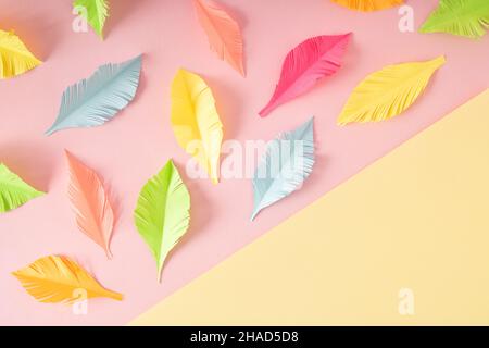Pastel colored cut feathers on creative  two-tone yellow-pink background. Flat lay colorful concept. Stock Photo