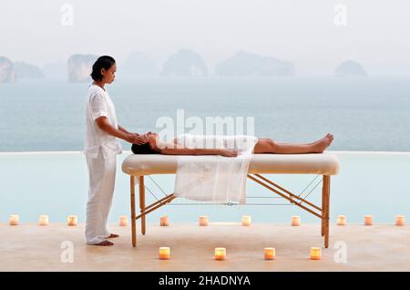 A woman receives a candlelit poolside massage at dusk at a  three-bedroom private pool villa. Yao Noi. Thailand. Stock Photo