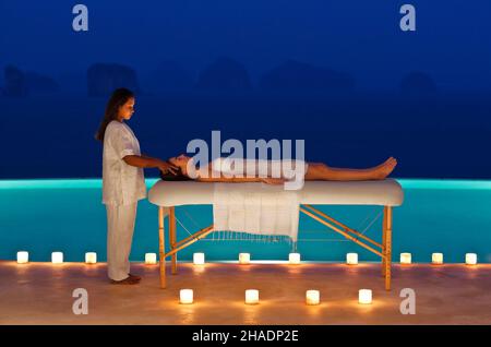 A woman receives a candlelit poolside massage at dusk at a  three-bedroom private pool villa. Yao Noi. Thailand. Stock Photo
