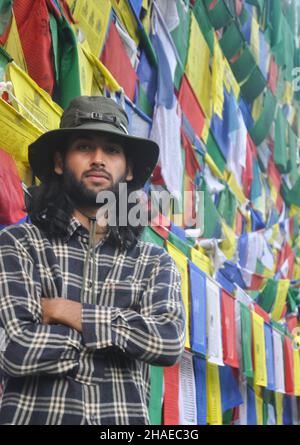 A good looking young guy looking at camera posing with his arms crossed, standing against Buddhist prayer flags Stock Photo